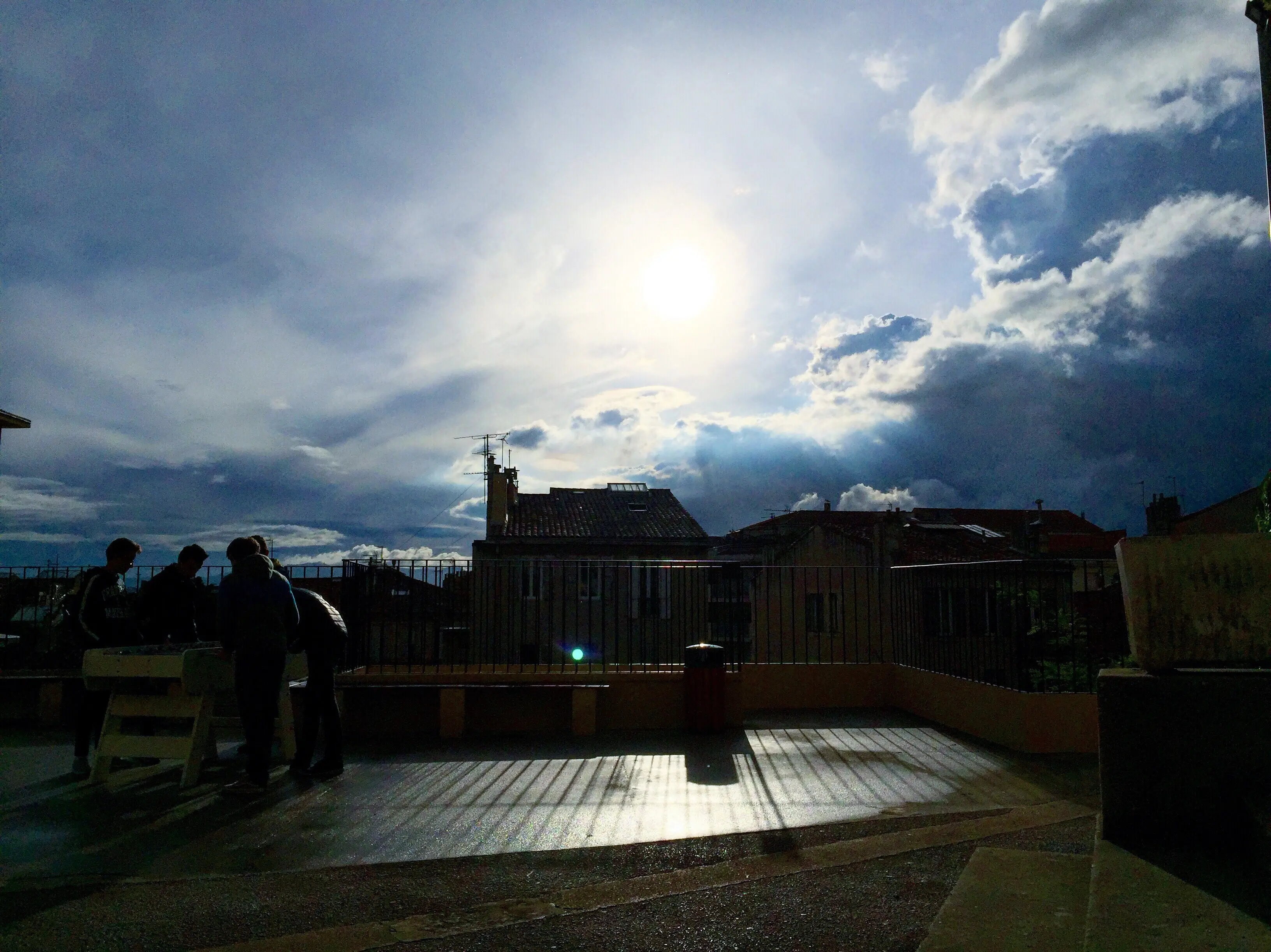 Freunde stehen an einem Tisch auf der Terrasse eines Gebäudes an einem sonnigen Tag.